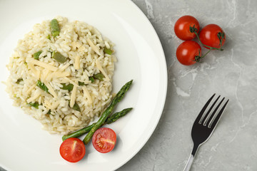 Delicious risotto with asparagus and tomatoes on grey marble table, flat lay