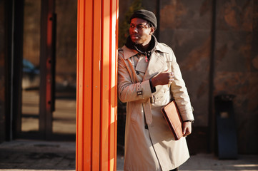 Handsome african american man posing outside in black hat and beige coat with folder in hand.