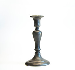 An antique metal candlestick stands on a table. On white background