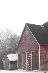 weathered wooden red barn on foggy winter morning