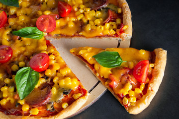 Tasty pizza with cherry tomatoes and sliced slice on a black background.