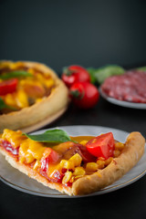 Slice of pizza with cherry and basil on a black background. Ingredients for preparing national Italian food.