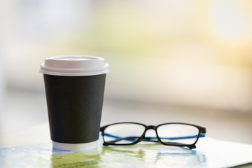 Close up of take away paper cup of hot coffee with reading glasses on world map with copy space.