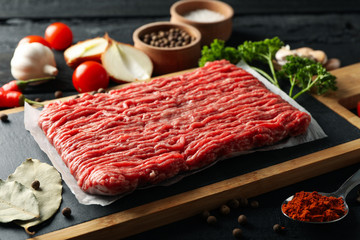 Spices and cutting board with minced meat on wooden background, close up
