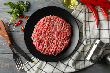 Spices and plate with minced meat on wooden background, top view