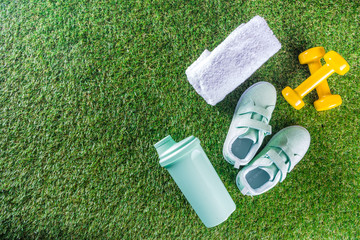 Summer sport, fitness, active lifestyle concept. Pastel sneakers, shaker for cocktail or water, towel, dumbbells. Fitness accessories for summer sport on green grass background flatlay copy space - obrazy, fototapety, plakaty