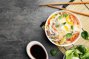 Tasty cooked rice noodles with vegetables served on grey table, flat lay. Space for text
