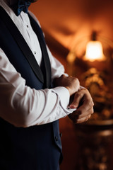 A groom fastens with a cufflink on the cuff of the sleeve of a luxurious white shirt. A man hand wearing a white shirt and cufflinks. Captures the groom cufflinks. Groom in fashionable suit