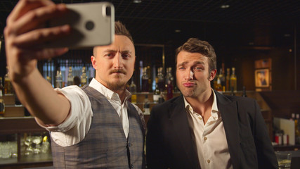 Two men stand at the bar and make a selfie on the phone