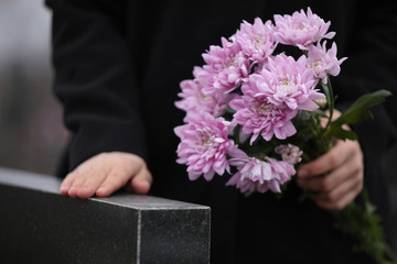 Woman holding chrysanthemum flowers near black granite tombstone outdoors, closeup. Funeral ceremony