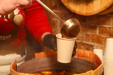 Obraz na płótnie Canvas Seller pouring tasty aromatic mulled wine into cup at winter fair, closeup