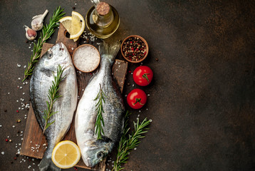 Fresh dorado fish with spices and ingredients tomato, razmorin, sunflower oil, lemon for cooking on a stone background with copy space for your text