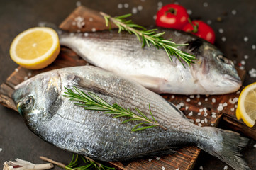 Fresh dorado fish with spices and ingredients tomato, razmorin, sunflower oil, lemon for cooking on a stone background