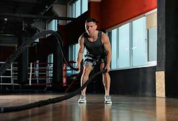 Fototapeta na wymiar Man working out with battle ropes in modern gym