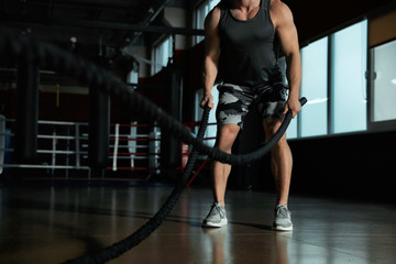 Fototapeta na wymiar Man working out with battle ropes in modern gym, closeup