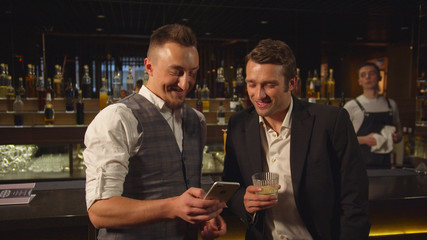 Two men stand at the bar and watch photos on the phone