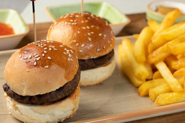 Small beef burgers with cereals bread, cheese,  served on a little cutting board with sauces, fries