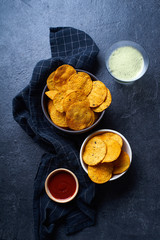  Mexican round-shaped nacho chips in two bowls with hot chili salsa and a glass of beer. Top view chips on dark background with copy space