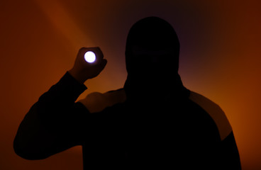 Blurred photo. Burglar in dark clothes holding the flashlight. Dangerous robber in mask with a...