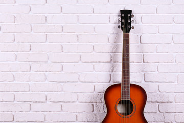 Fototapeta na wymiar Folk style parlor acoustic guitar over white brick wall background with a lot of copy space for text. Studio shot of travel size musical instrument. Close up.