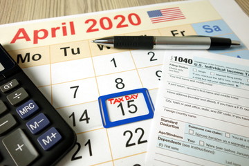 Tax day marked on April 2020 monthly calendar with 1040 form pen and calculator