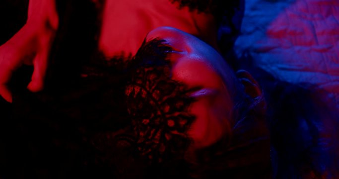 smiling face of young woman, playing with black lace in bed, closeup of head in darkness