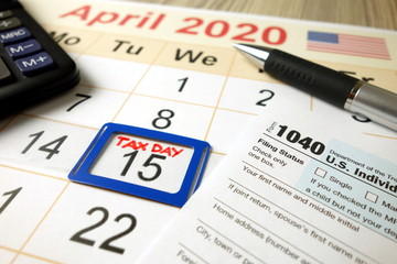 Monthly calendar showing date April 15th 2020 marked as tax day with 1040 form pen and calculator