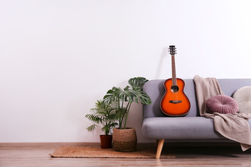 Minimalistic interior design concept. Acoustic guitar on grey textile sofa in spacious room of loft...