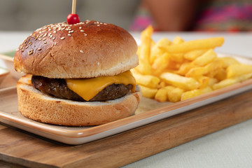 Small beef burgers with cereals bread, cheese,  served on a little cutting board with sauces, fries