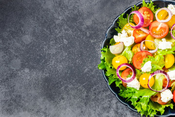 Tomatoes feta cheese green salad on dark background. Top view, space for text.