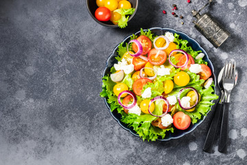 Tomatoes feta cheese green salad on dark background. Top view, space for text.