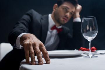 Selective focus of elegant man with hand by head sitting at served table isolated on black