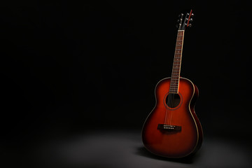 Folk style parlor acoustic guitar in darkness on black background with a lot of copy space for text. Studio shot of travel size musical instrument. Close up. - obrazy, fototapety, plakaty