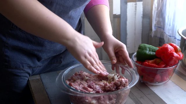 beautiful mature woman in pink sweater and in economic apron stuffs bell peppers with fresh minced pork. girl cuts pepper, onion, prepares sauce and puts minced meat in peppers
