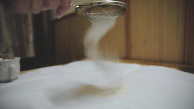 Baker sifting wheaten flour and preparing dough for making cake