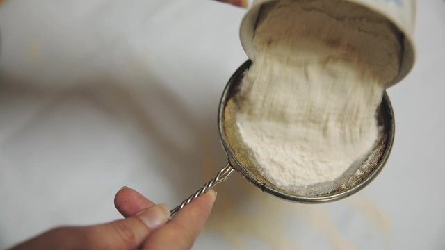 Baker sifting wheaten flour and preparing dough for making cake