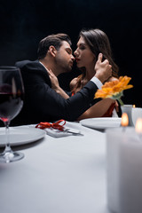 Selective focus of elegant couple kissing during romantic dinner isolated on black