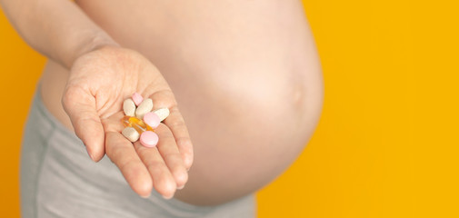 Beautiful young pregnant woman holds vitamins pills tablets in her hand on yellow background selective focus copy space. Pregnant Health Concept, expectation of the child, pregnancy and motherhood