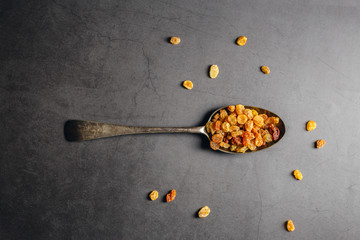 Dried raisins on a spoon over black marble background
