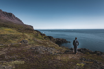 Fototapeta premium Young man hiker in the arctic landscape of Disko Bay in Greeland in Summer. Blue Sky and green meadows. Arctic Circle Trail with temple mountains. Disko Island and Village of Qeqertarsuaq,