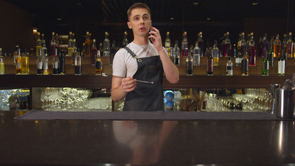 Bartender talks on the phone and plays with spoon at the bar