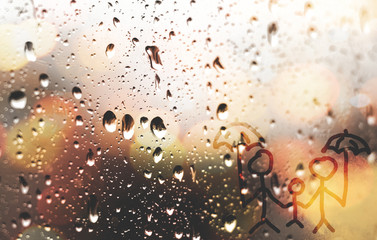A family together with umbrellas is painted with a finger on the misted glass during the rain. Drawing on glass in drops.