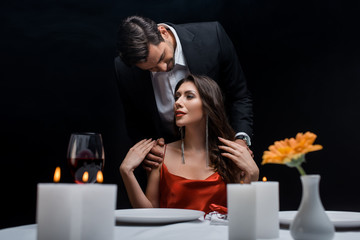 Selective focus of man in suit hugging beautiful girlfriend during romantic dinner isolated on black