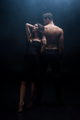 Full length of sexy woman standing by back of muscular man on black background with smoke