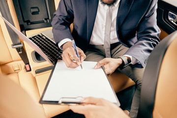 Close up of a man signing papers clipped to a notepad.