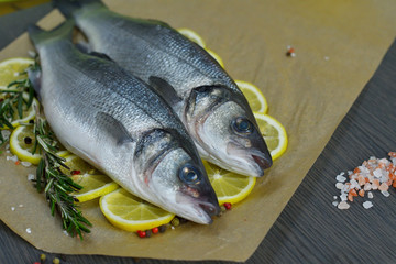 Raw fish seabass. Two Raw fish fillet with spices, herbs, lemon and salt on paper dark background ready for cooking, food background. Healthy food concept. Mediterranean seafood