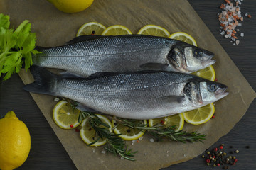 Raw fish seabass. Two Raw fish fillet with spices, herbs, lemon and salt on paper dark background ready for cooking, food background. Healthy food concept. Mediterranean seafood