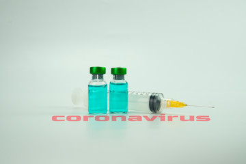 Green liquid vials and syringe on white background. Medical health concept. Text Coronavirus in red.
