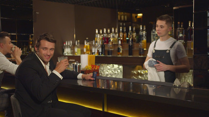 Man sits at the bar, talks to bartender and smiles to someone