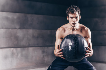 Strong handsome man workout with wall ball in dark gym.